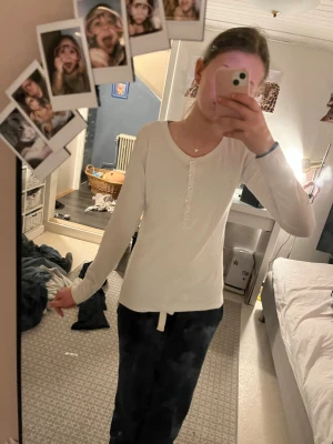 Vit långärmad topp med knappar - Säljer en enkel och stilren vit långärmad topp med knappar framtill och knyt i nederkanten. Toppen har en v-ringad hals och är gjord i mjukt bomullsmaterial. Perfekt till jeans eller kjol för en clean look.