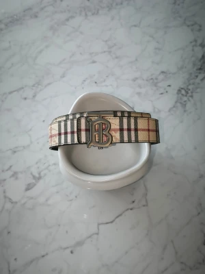 Burberry bälte med silvrigt märke - Tvär fett bälte från Burberry, väldigt enkel att styla och har en unik "funktion", man kan vända bältet ut o in och byta sida på loggan. Det gör att bältet då blir svart och på bild tre så kan du se hur det kommer att se ut (loggan blir också på den sidan)  