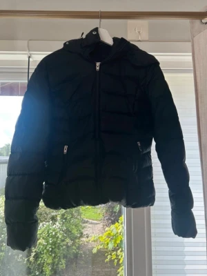 Svart kort pufferjacka med huva - En mycket fin vinterjackan ifrån rockandblue Kort.  Använt en del men är fin bevarad, finns inga hål eller tecken på användning.  Dunjacka Tillkommer fuskpäls krage(vit med svart i sig.)  Två innerfickor med dragkedja  Dragkedjan funkar utan problem.  Passar M/L