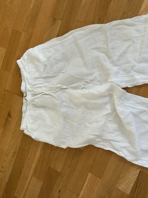 Vita linnebyxor med dragsko - Säljer ett par luftiga vita linnebyxor med resår i midjan och dragsko för skön passform. Byxorna har raka ben och är perfekta för en avslappnad och stilren look. Materialet är tunt och svalt linne, vilket gör dem riktigt bekväma.