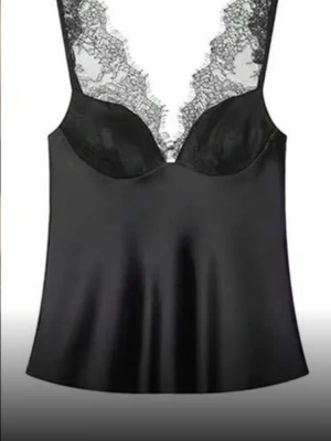 Svart satinlinnetopp med spets - Stilren svart linnetopp i satin med vacker spetsdetalj vid urringningen och axelbanden. Toppen har en lätt glansig finish och en feminin siluett som ger en elegant look. Perfekt att styla med jeans eller kjol för en trendig outfit.