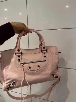 Balenciaga city bag petal pink - Säljer min  supersnygga city bag i färgen petal pink från Balenciaga. Färgen är i ljusrosa färg och i äkta skinn. Den är använd men fortfarande i fint skick inga defekter. Säljs då den inte kommer så mycket till användning, hoppas den hittar ett nytt hem🩷