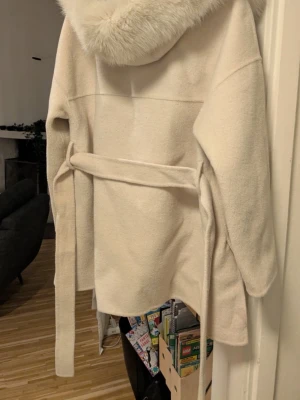 Vit kappa med päls detaljer  - hej! Säljer nu min fina kappa från FUR Stockholm, eftersom den inte kommer till användning längre tyvärr:/ men den är i jätte fint skick använd ett par gånger men typ som ny, (ena bilden är från hemsidan, skriv till mig för bilder på jackan☺️) pris kan diskuteras💓