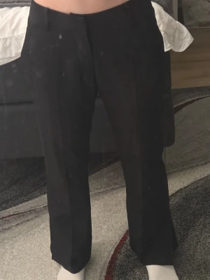Svarta raka kostymbyxor - Säljer ett par svarta kostymbyxor med rak passform och pressveck. Byxorna har hög midja och klassisk design, perfekta för en stilren look. Materialet känns mjukt och följsamt, vilket ger en snygg siluett.