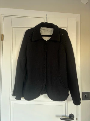 Svart stickad jacka - Svart stickad kofta/jacka med klassisk krage och lång ärm. Koftan/jackan har en enkel design med diskreta detaljer och ficka framtill. Är i storlek m men funkar bra om man har S i andra kläder!