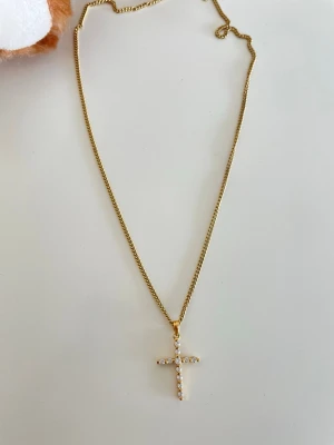 Guldhalsband med kors och pärlor/ guldpläterad guldfynd  - Snyggt halsband i guldfärg med ett korsformat hänge dekorerat med små vita pärlor. Kedjan är tunn och elegant, vilket gör att hänget verkligen står ut. Perfekt accessoar för dig som gillar stilrena smycken med en twist.
