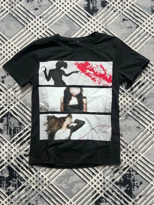 Svart t-shirt med grafiskt tryck - Cool svart t-shirt med ett stort grafiskt tryck på framsidan i tre paneler med siluetter och färgstänk i rött och vitt. Klassisk rund hals och korta ärmar. Perfekt för dig som gillar unika motiv och streetwear-vibe.