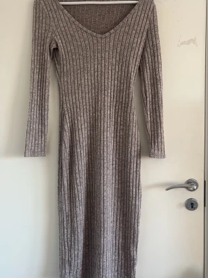 Beige ribbad långklänning - Säljer en beige ribbad långklänning med v-ringning och långa ärmar. Klänningen är i storlek S men den sätter sig fint även om de är i storlek M. Använd bara några gånger 