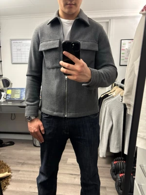 Mörkgrå jack overshirt med dragkedja - Stilren mörkgrå overshirt med dragkedja framtill och två stora bröstfickor. Overshirten har klassisk krage och raka ärmar med knapp vid manschetten. Tillverkad i ett tjockare, mjukt material som ger en clean look. Perfekt att bära över en t-shirt.