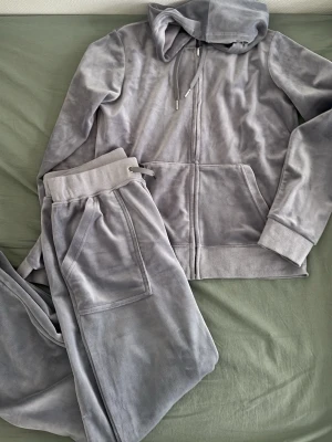 Grått velour loungewear-set - Mysigt loungewear-set i mjuk grå velour med zip-hoodie och matchande byxor. Hoodien har dragkedja, fickor och huva, medan byxorna har bred resårmidja med snörning och fickor fram. Perfekt för chill dagar hemma. I CAN ALSO SELL JUST ONE OF THE PAIR