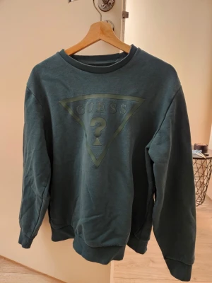 Sweatshirt från Guess - Mörkgrön sweatshirt från Guess med det klassiska triangellogot på bröstet. Storleken på etiketten är XL, men enligt min mening passar den bättre för storlek L.