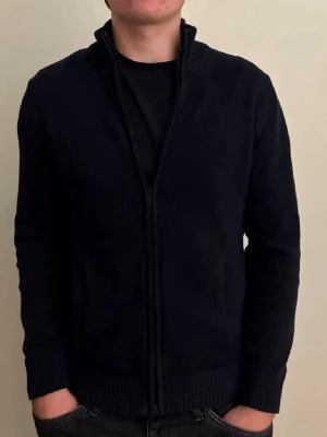 Mörkblå stickad ziptröja - Mörkblå stickad tröja med dragkedja framtill och hög krage. Tröjan är i jättefin skick och har inga defekter alls.