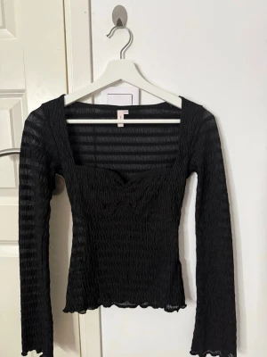 Svart ribbad topp från Nelly - Säljer en svart ribbad långärmad topp från Nelly med fyrkantig ringning och subtila volangdetaljer vid ärmslut och nederkant. Använd en gång och Pris kan diskuteras 