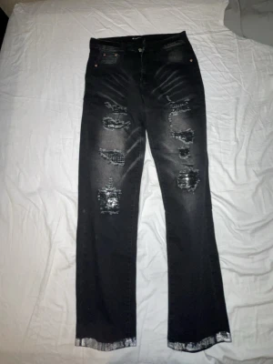Svarta slitna jeans med raka ben - Säljer ett par svarta jeans med raka ben och tydliga slitningar framtill. Jeansen har en klassisk femficksmodell och råa kanter vid bensluten. Perfekta för en avslappnad och trendig look.
