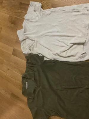 Två basic t-shirts i vitt och grönt - Säljer två enkla t-shirts, en i vit och en i olivgrön färg. Båda har rund halsringning och korta ärmar. Perfekta till vardags och lätta att matcha med jeans eller shorts.