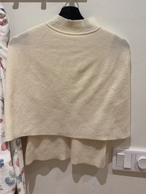 Vit polotröja i mjuk stickning - Säljer en vit polotröja i mjuk, ribbstickad kvalitet. Tröjan har en hög krage och avslappnad passform med något kortare längd. Perfekt för lager på lager och enkel att matcha med olika stilar.