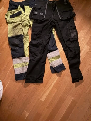 Arbetsbyxor-Paket - Här är ett paket med arbetsbyxor i olika färger. Byxorna har flera fickor och detaljer.  - Storlek 48 båda två  - Nytt svart byxor - Gröna byxor inte nytt men det är bra skick  - Båda två samma pris