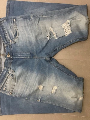 Ljusblå slitna jeans med hål - Säljer ett par ljusblå jeans med trendiga slitningar och hål på både fram- och baksida. Klassisk femficksmodell med knapp och dragkedja. Jeansen har en avslappnad passform och är tillverkade i denim med snygg tvättad look. Jeansen är i mycket bra skick och säljs för ett bra pris! Skriv vid minsta fundering!!🤩🤩