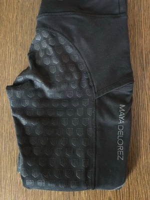 Svarta ridtights från Maya Delorez - Snygga svarta ridtights från Maya Delorez med silikonmönster för extra grepp. Tightsen har hög midja och är tillverkade i stretchigt funktionsmaterial som andas. Märkeslogga längs benet och smarta sömmar för bästa passform. Perfekta för träning och ridning. I använt skick men inget sönder eller trasigt. 