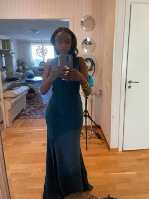 Balklänning - Elegant mörkblå långklänning med figurnära passform och slits på sidan. Klänningen är ärmlös och har en stilren, enkel design som framhäver siluetten. Perfekt för bal eller festliga tillfällen.