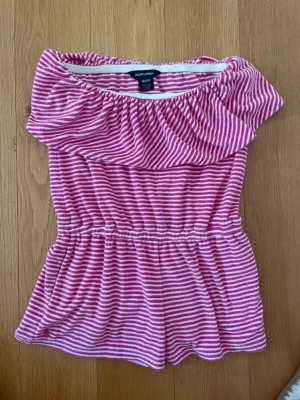 Rosa randig jumpsuit från Ralph Lauren - Supersöt rosa och vit randig jumpsuit från Ralph Lauren med off-shoulder design och resår i midjan. Superfint skick, använt gåtal gånger i storlek M 8/10 år🌟