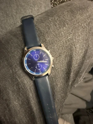 Blå analog klocka med läderband - Stilren klocka med blå urtavla och matchande blått läderband. Klockan har silverfärgat boett och detaljer, samt två mindre urtavlor för extra funktioner. Perfekt accessoar för dig som gillar klassisk men modern stil.