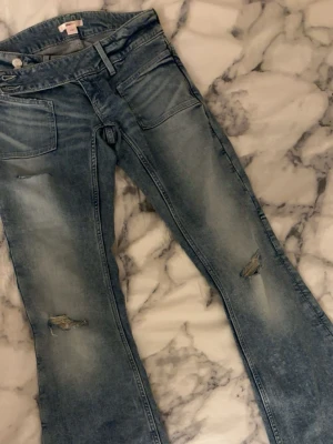 Blå slitna bootcut jeans - Säljer ett par ljusblå bootcut jeans med slitningar på benen och stora framfickor.Perfekta för en avslappnad och trendig look.                          ALDRIG ANVÄNDA 💞💞