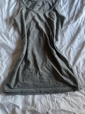 Grå  linnetopp - Säljer en enkel och stilren grå linnetopp i 80% bomull. Toppen har en figurnära passform och är ärmlös med klassisk rund halsringning. Perfekt att matcha med jeans eller shorts för en clean look.