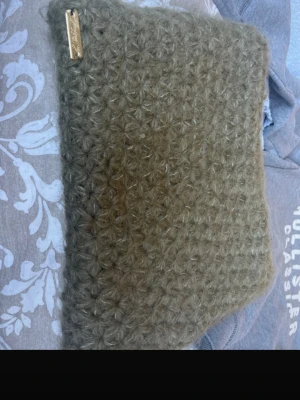 Olivgrön stickad datorväska - Säljer en olivgrön datorväska från CrochetUf Väskan är handstickad i fluffigt garn med ett unikt mönster och har en liten metallbricka med märkesnamnet. Perfekt accessoar för dig som gillar en personlig och mysig stil. 