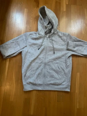 Ljusgrå zip hoodie med huva - Säljer en ljusgrå hoodie med dragkedja och stor huva. Hoodien har dragsko i huvan, två stora fickor framtill och ribbade muddar vid ärmslut och nederkant. Perfekt för chill dagar och enkel att matcha med jeans eller mjukisbyxor.