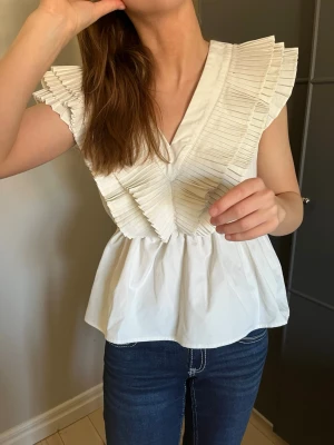 Vit blus med plisserade volanger - Intressekoll på denna supersnygga v-ringade volangtoppen från Vero Moda. 