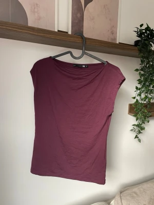 Vinröd topp ärmlös  - En enkel och stilren mörklila topp. Toppen har en lös passform, är ärmlös och har en rund halsringning. Tillverkad i mjuk bomull som känns skön mot huden. Perfekt att matcha med jeans eller kjol för en avslappnad look.