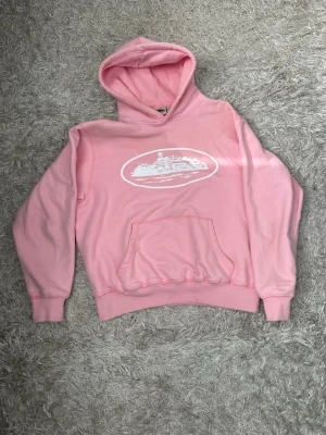 Rosa corteiz hoodie - Snygg rosa corteiz hoodie med vit illustration på bröstet. Hoodien har en klassisk känguruficka och ribbade muddar vid ärmar och midja. Tillverkad i mjukt material som känns skönt mot huden. Perfekt för en avslappnad och trendig look, som passar perfekt med de matchande byxorna. Hela settet/tracksuiten finns i min profil som en egen annons.