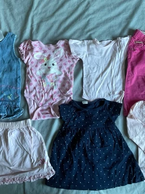 Bundle med olika sorters babykläder i storlekarna 80-86 - Säljer två gulliga babybodys, en ljusrosa med rosa prickar och kaninmotiv samt texten 'My cute bunny', och en helt vit body. Båda har korta ärmar och tryckknappar i grenen för enkel påklädning. Perfekta för små barn och tillverkade i mjukt bomullstyg.