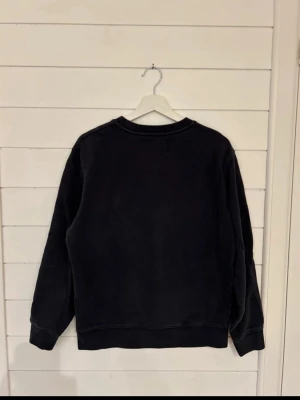 Svart sweatshirt från Replay - En stilren svart sweatshirt från Replay med rund halsringning och ribbade muddar vid ärmslut och nederkant. Perfekt för en avslappnad look och enkel att matcha med jeans eller byxor. Klassisk passform och mjukt material.