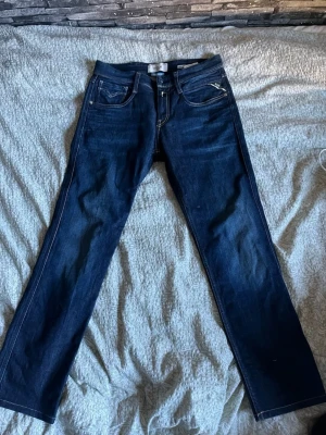 Mörkblå jeans från Replay - Snygga mörkblå jeans från Replay med raka ben och klassisk femficksmodell. Jeansen har kontrastsömmar och en läderpatch med Replay-logga bak i midjan. Perfekta för dig som gillar stilrena och tidlösa jeans.