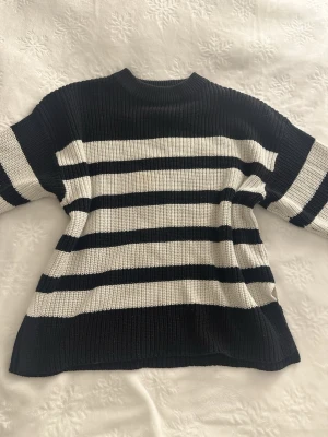 Svartvit randig stickad tröja - Stickad tröja med breda svarta och vita horisontella ränder. Tröjan har rund halsringning, långa ärmar och ribbstickade muddar. Materialet är mjukt och tjockt, Klassisk och enkel design som passar till det mesta.