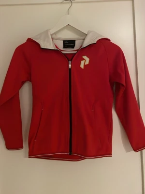 Röd hoodie från Peak Performance - Snygg röd hoodie från Peak Performance. Snygg logga på bröstet och en zip. Storlek 140 junior.  