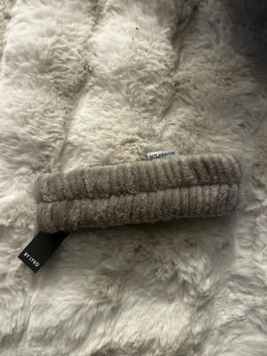 Beige fluffigt hårband från Lyko - Mysigt och fluffigt hårband i beige färg från Lyko. Tillverkat av 95% polyester, perfekt för att hålla håret borta vid sminkning eller hudvårdsrutiner. Hårbandet har en ribbad struktur och känns supermjukt mot huden.