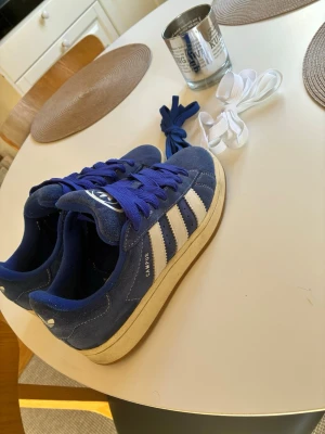 Blå Adidas Campus sneakers 40/2/3 - Säljer ett par blå Adidas Campus sneakers i mocka med klassiska vita ränder på sidorna, storlek 40/2/3