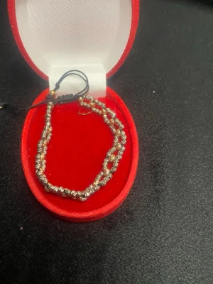 Silvrigt flätat armband med pärlor - Snyggt armband med dubbla rader av små silverfärgade pärlor och diskreta gulddetaljer. Armbandet har en svart justerbar snörning som gör det enkelt att anpassa storleken. Perfekt accessoar för att lyfta din stil.