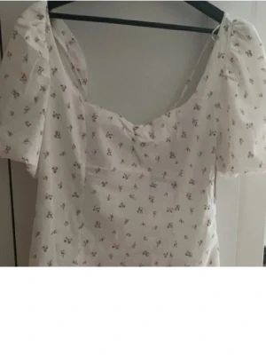 Sommarklänning - Charmig vit klänning med små rosa blommor och puffiga kortärmar. Den har en söt, romantisk stil med en lätt och luftig känsla. Perfekt för varma dagar och somriga tillfällen💗