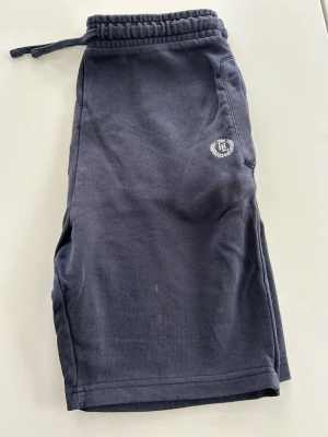 Mörkblå shorts med snörning - Mörkblå shorts från Henri Lloyd med elastisk midja och snörning. Mjuk bomullskvalitet och diskret logga broderad på ena sidan. Perfekta för chill dagar eller träning.