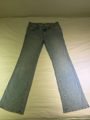 Ljusblå bootcut jeans - Säljer ett par ljusblå bootcut jeans i klassisk denim med fem fickor och normal midja. Jeansen har en avslappnad passform med lätt utsvängda ben och tidlös look. Perfekta till sneakers eller boots för en trendig vardagsstil.