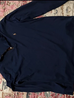 Mörkblå långärmad skjorta Polo Ralph Lauren - Klassisk mörkblå långärmad skjorta från Polo Ralph Lauren med den ikoniska broderade loggan på bröstet. Skjortan har knappar vid kragen och är tillverkad i mjukt bomullsmaterial. Perfekt för en stilren och avslappnad look.