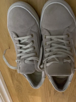 Beige mockasneakers med vita sulor - Snygga beige sneakers från Vagabond i mocka med vita, tjocka gummisulor och matchande vita skosnören. Klassisk låg modell med diskreta detaljer och metallöljetter. Perfekta för dig som gillar stilrena och neutrala färger. Storlek 39.