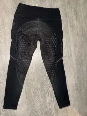 Svarta fodrade vinter leggings från Maya Delorez  - Säljer ett par svarta ridtights från MADDOX med helskoning i silikon för extra grepp. Tightsen har hög midja och stretchigt material som ger bra rörelsefrihet. Perfekta för ridning och träning. Snyggt mönster på silikonet och diskret logga på sidan.