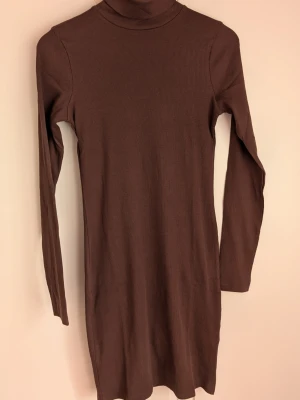 BIK bok Brun ribbad poloklänning Storlek M - Brun ribbad klänning med polokrage och lång ärm. Klänningen har en rak passform och är tillverkad i ett stretchigt material som ger en bekväm och stilren look.