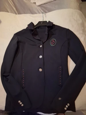 Fin tävlingskavaj storlek 152 - Väldigt fin tävlingskavaj med rosa kristaller till den unga ryttaren. Knappt använd.