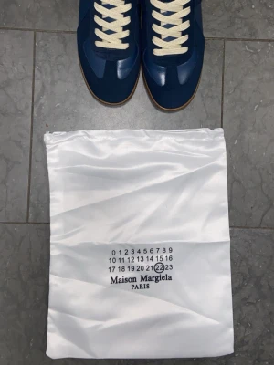 Mörblå Skor - Snygga sneakers i mörkblå mocka kombinerat med ljusblått skinn som ger en stilren men ändå levande look. De vita snörena bryter av snyggt och förstärker den klassiska retrokänslan. Modellen har en låg profil och en tidlös design som passar lika bra till jeans som till mer uppklädda, avslappnade outfits. Observera att skicket är bra och att dem har använts flera gånger. Bilderna är för när dem var nya. Skicka Dm om du vill ha fler bilder.